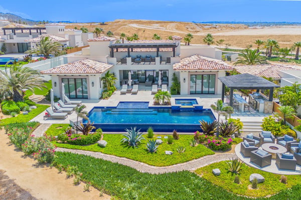 Resort with yellow buildings, palm trees, and curved pools overlooking blue ocean with rocky islands