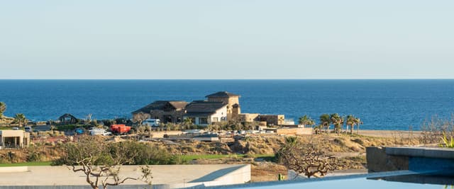 Covered terrace with rectangular swimming pool, stone walls, and panoramic sea view overlooking coastal landscape